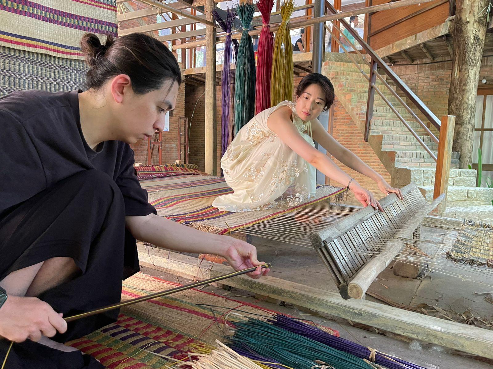 Visitors weaving a reed mat on the traditional loom